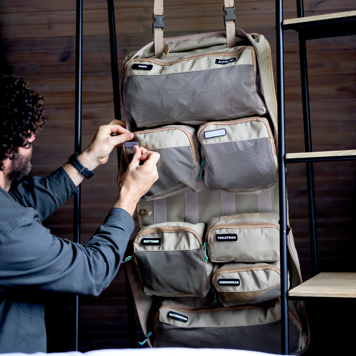 Man packing an XPLR Duffel modular travel bag hung on a rack