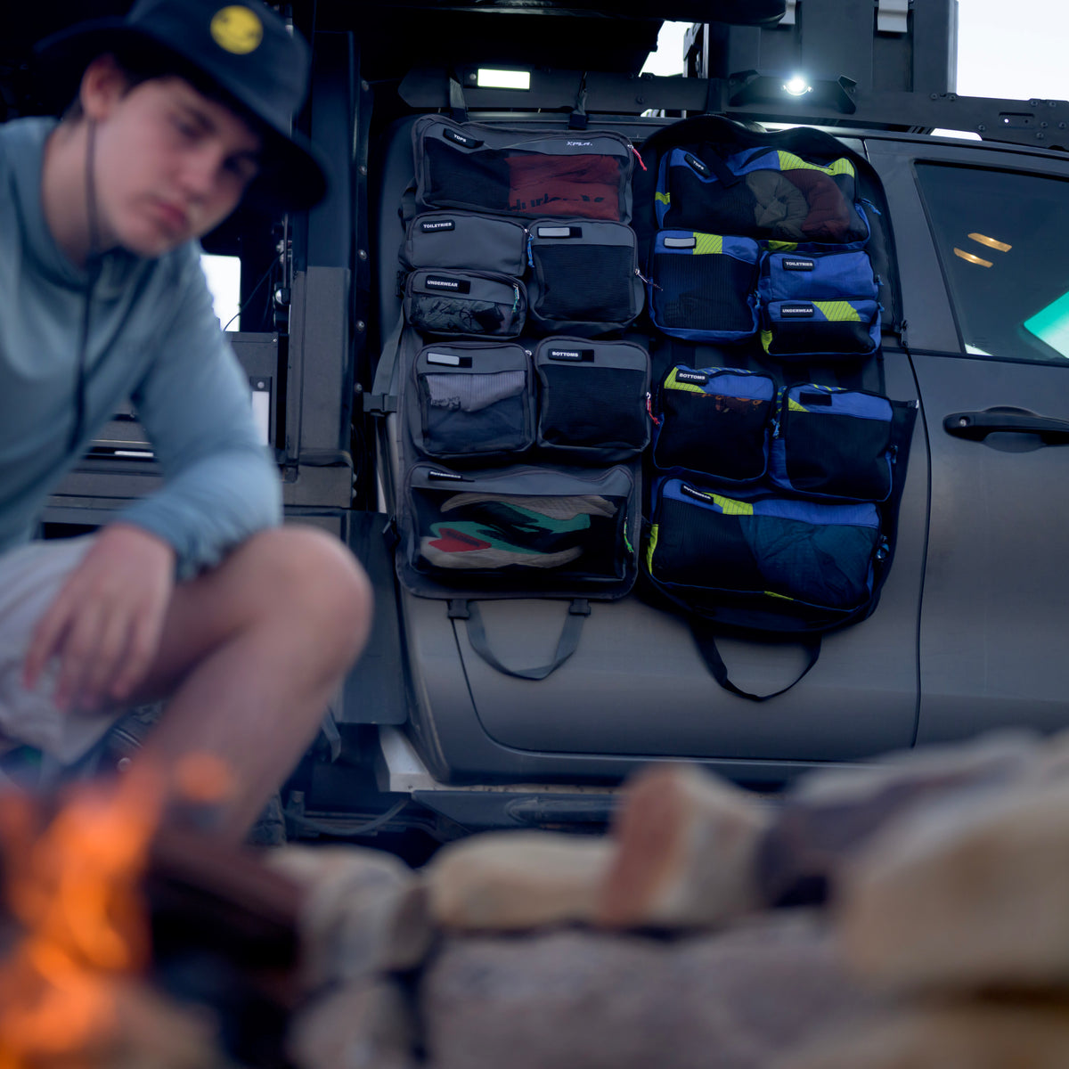 XPLR modular hanging travel bag with pockets hung on a vehicle door beside a campfire