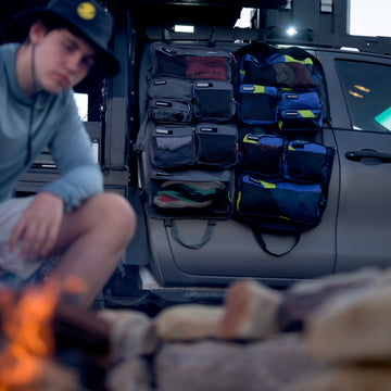 XPLR modular hanging travel bag with pockets hung on a vehicle door beside a campfire