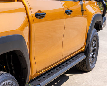 IRONMAN 4x4 premium side steps on an orange Toyota Hilux Travo, side view