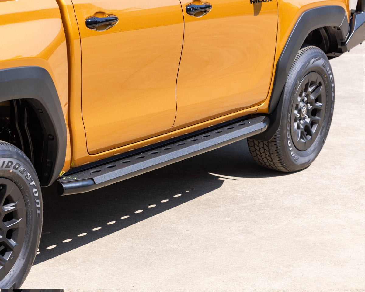 IRONMAN 4x4 black side steps fitted to an orange Toyota Hilux Travo