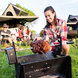 Woman cooking meat on the IRONMAN 4x4 rotisserie kit over a portable fire pit at camp