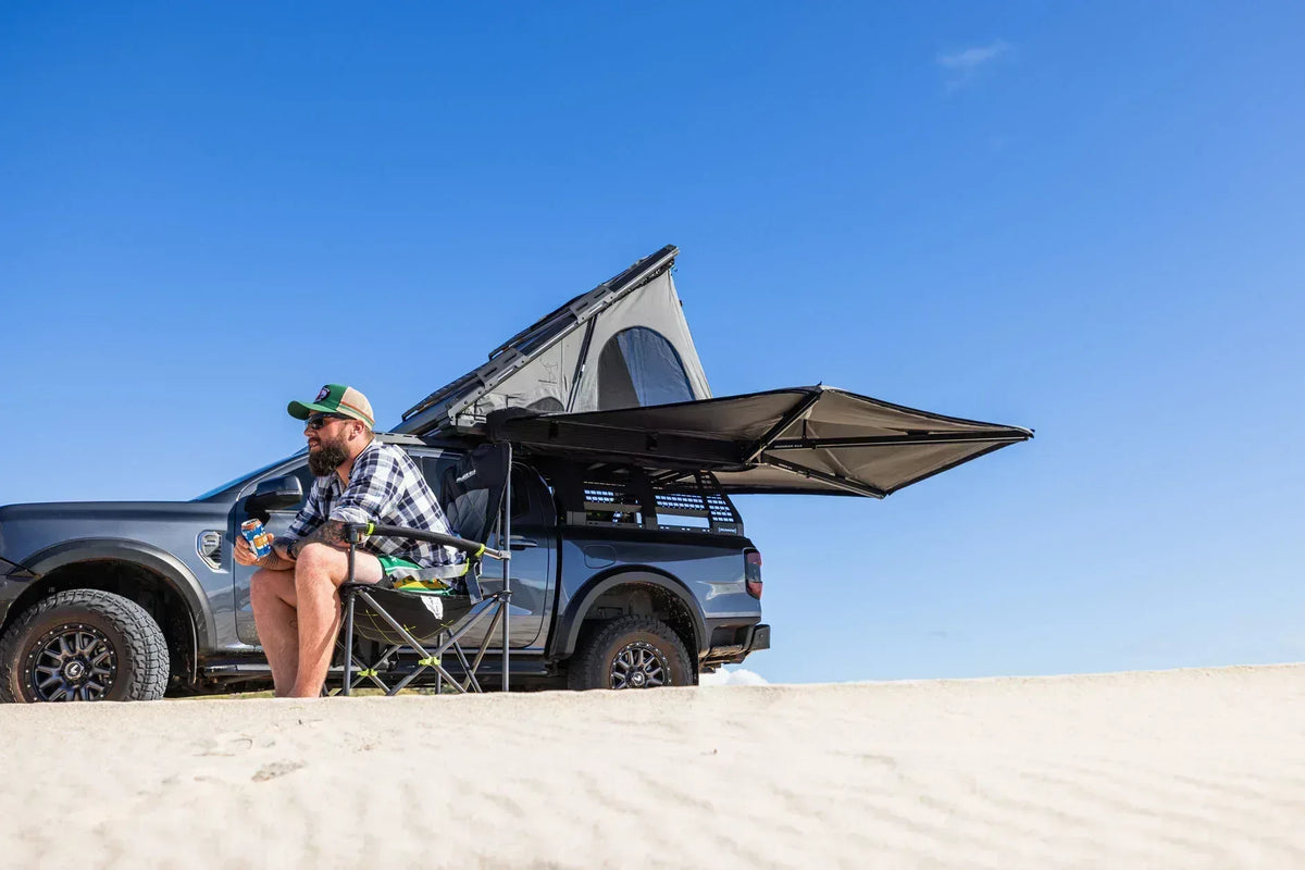 Man relaxing in a camp chair under a Deltawing 270 degree awning on a 4x4 at the beach