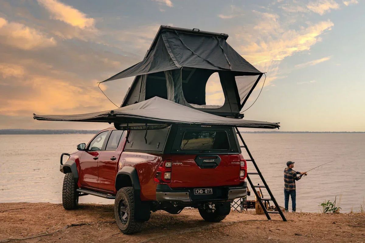 Red bakkie with rooftop tent and Deltawing 270 degree awning at a lakeside camp at sunset