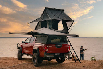 Red bakkie with rooftop tent and Deltawing 270 degree awning at a lakeside camp at sunset