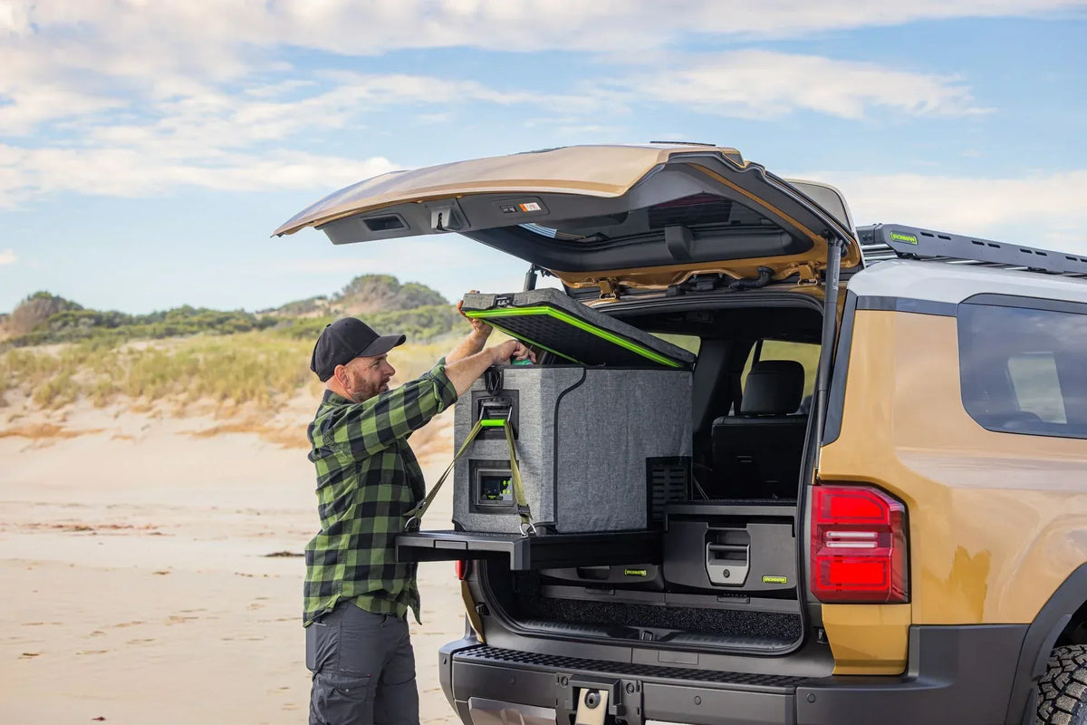 Man loading a fridge onto an IRONMAN 4x4 drawer slide in a Toyota Prado 250 at the beach