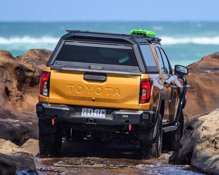 IRONMAN 4x4 rear protection tow bar fitted to an orange Toyota Hilux Travo, rear view at the coast