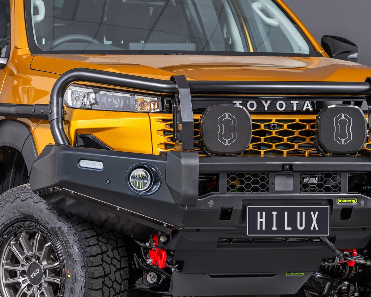 Close-up of the IRONMAN 4x4 Deluxe bull bar fitted to an orange Toyota Hilux Travo with driving lights